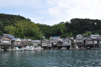 海沿いに昔ながらの舟屋が並んでおり、数隻の漁船が舟屋の前に停泊している写真