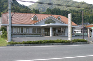建物前に駐車場があり、オレンジ色の屋根をした伊根町国民健康保険本庄診療所の外観写真
