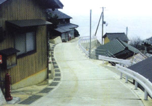 住宅横の道路が綺麗に舗装され、なだらかな下り坂になっている道路工事後の集落環境の写真