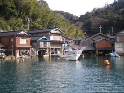 海に一隻の漁船が停まっており海沿いに舟屋が並んでいる海から見た舟屋のまちなみの写真